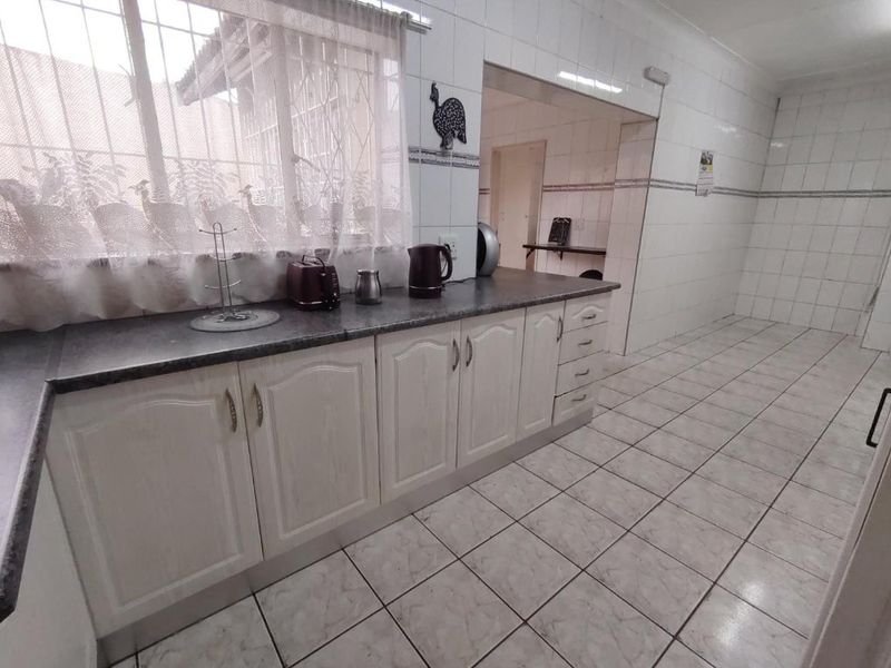 A functional kitchen featuring white cabinetry, laminate countertops, and fully tiled walls and floors, with an adjacent scullery or utility area.