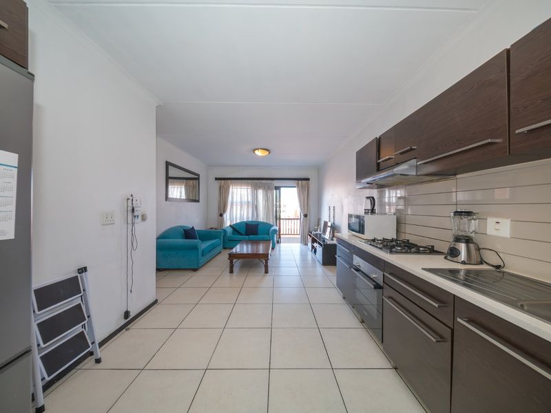 Open-plan living area featuring a galley-style kitchen with dark wood cabinetry, gas hob, and tiled flooring, leading to a balcony.