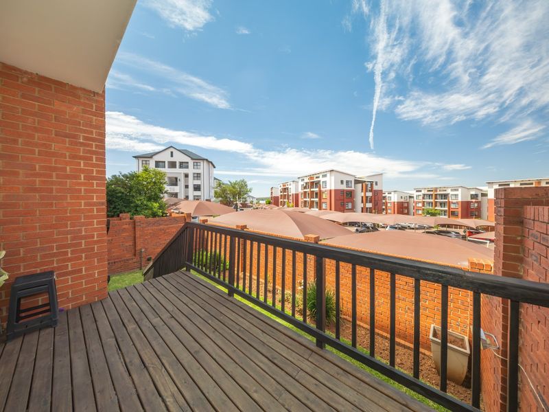 An elevated timber balcony featuring a wooden balustrade, overlooking the complex grounds and surrounding residential apartment buildings.