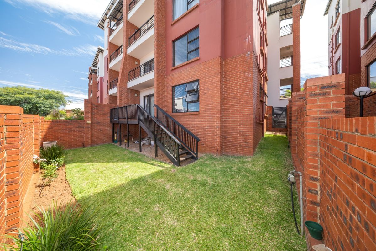 A private rear garden area featuring a lawn, brick boundary walls, and a timber staircase leading to an elevated balcony.