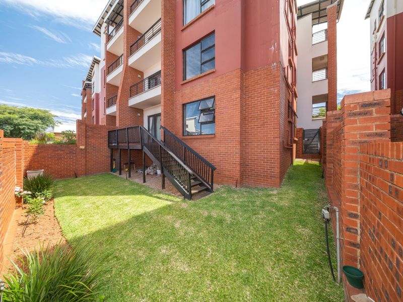 A private rear garden area featuring a lawn, brick boundary walls, and a timber staircase leading to an elevated balcony.