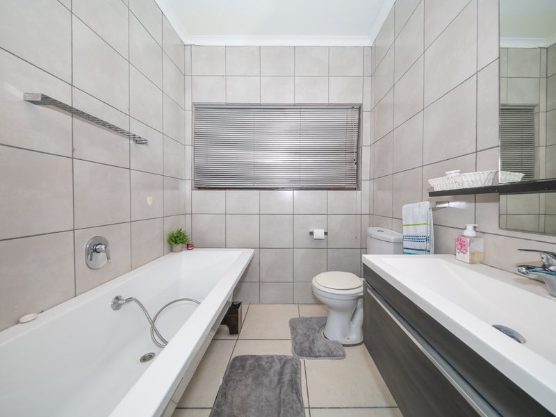A clean and functional bathroom featuring a bathtub, vanity with basin, toilet, and neutral wall-to-floor tiling.