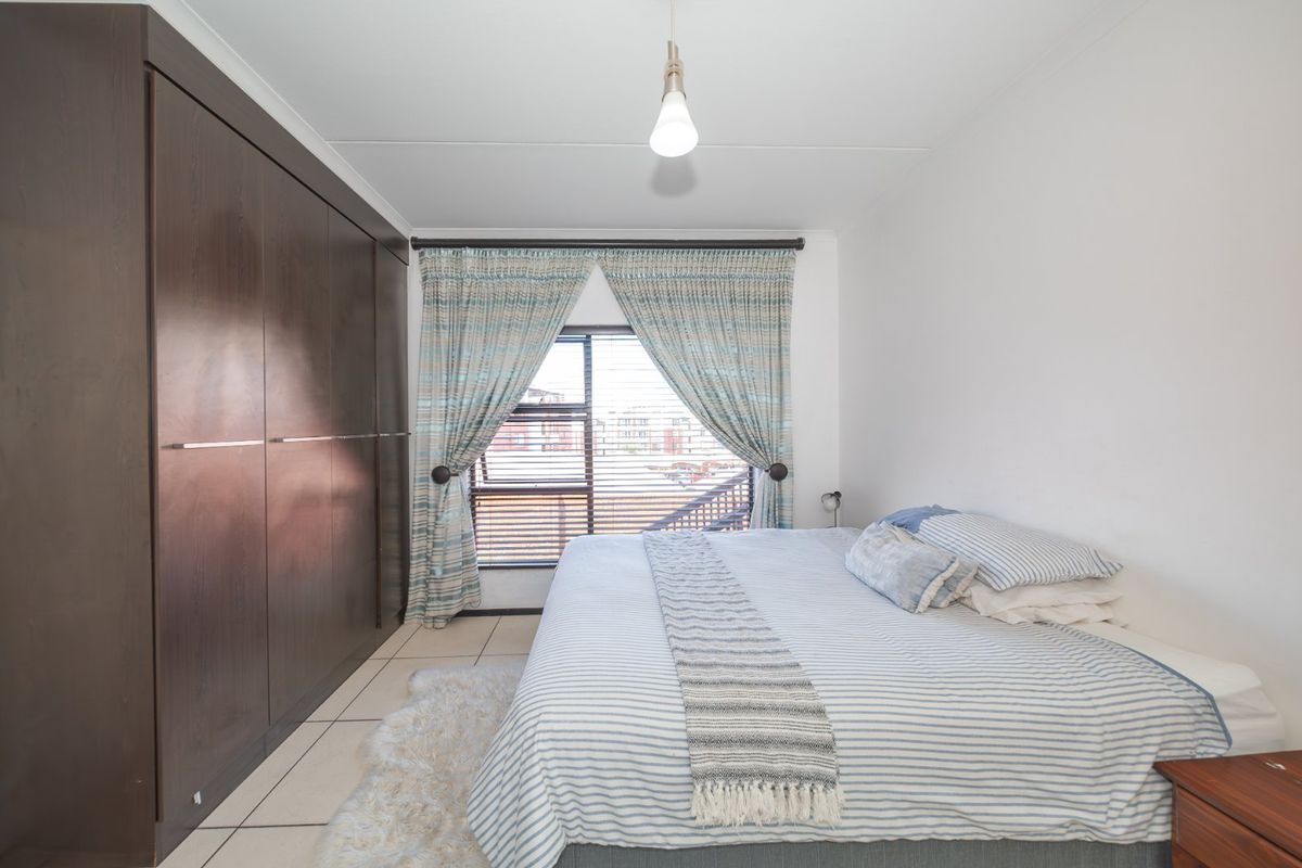 A well-maintained bedroom featuring dark wood built-in cupboards, tiled flooring, and a window with fitted blinds.