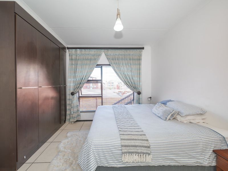 A well-maintained bedroom featuring dark wood built-in cupboards, tiled flooring, and a window with fitted blinds.