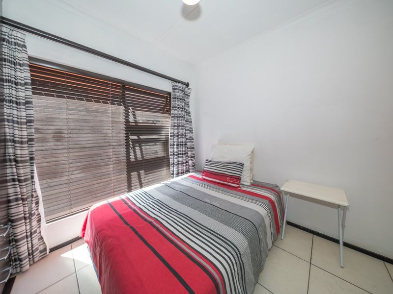 A functional bedroom featuring tiled flooring, a built-in wardrobe, and venetian blinds, offering a clean and simple space.