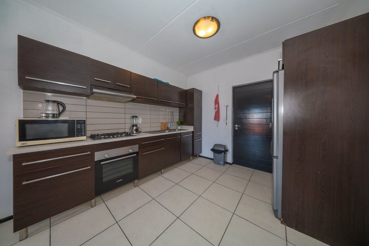 A functional kitchen featuring dark wood cabinetry, a gas hob, built-in oven, extractor fan, and neutral tiled flooring.