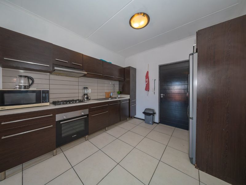 A functional kitchen featuring dark wood cabinetry, a gas hob, built-in oven, extractor fan, and neutral tiled flooring.