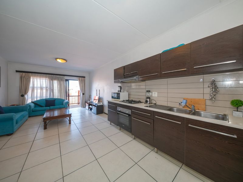 Open-plan living area featuring a modern kitchen with dark wood cabinetry, gas hob, and tiled flooring, leading to a balcony through sliding doors.