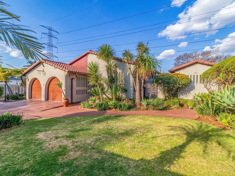 Front view of a house featuring a double garage with arched doors, a brick-paved driveway, and a well-maintained landscaped garden.