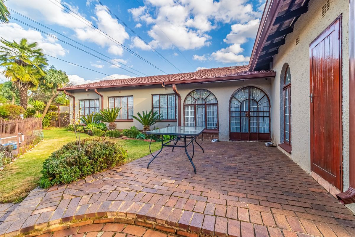 A well-maintained rear exterior featuring a brick-paved patio, arched glass doors, and a landscaped garden area under a tiled roof.