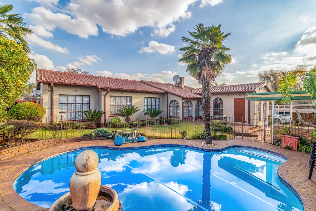 Rear view of the house featuring a swimming pool, paved patio area, and landscaped garden with established palm trees.