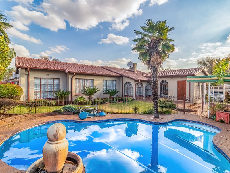 Rear view of the house featuring a swimming pool, paved patio area, and landscaped garden with established palm trees.