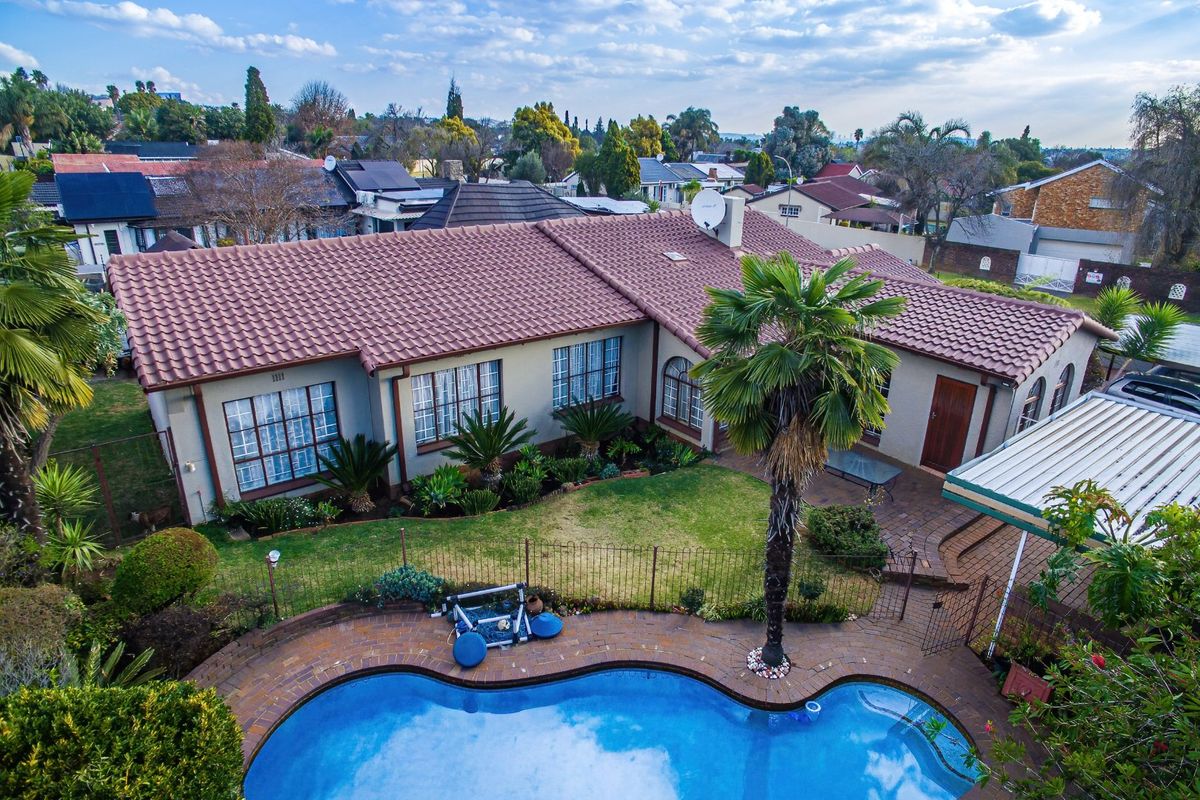 Aerial view of a residential property featuring a tiled roof, a swimming pool, a paved patio area, and a well-maintained garden.