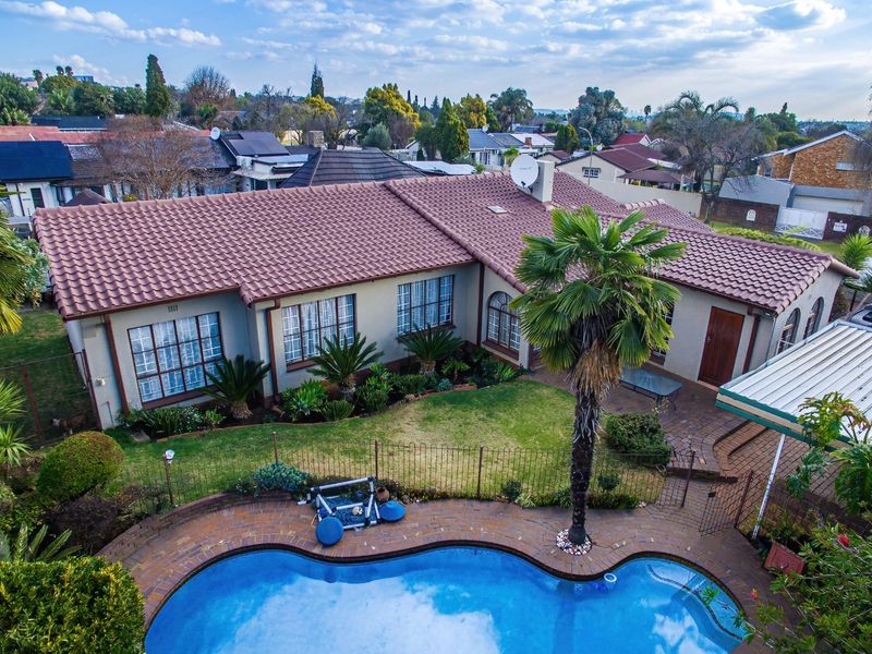 Aerial view of a residential property featuring a tiled roof, a swimming pool, a paved patio area, and a well-maintained garden.
