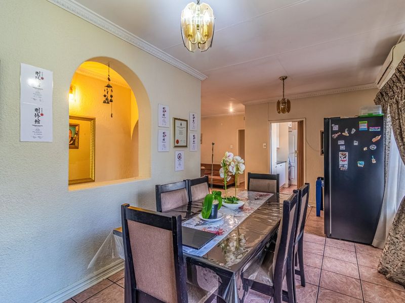 A dining room featuring tiled flooring, coved cornicing, and a decorative archway leading to an adjacent living space.