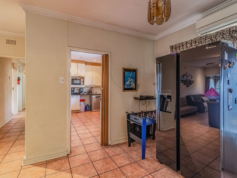 Open plan living area featuring tiled flooring, ceiling cornicing, and an integrated air conditioning unit, with a view through to the kitchen.