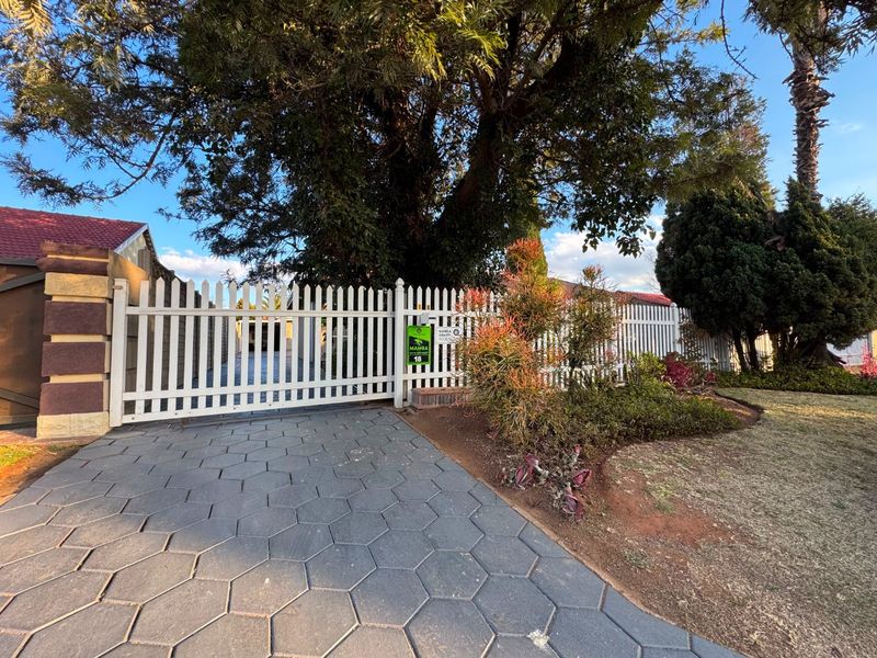 Front view of the property featuring a white picket fence, secure gated entrance, and a paved driveway leading to the home.