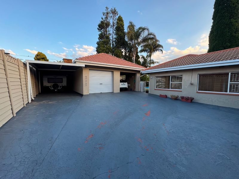 Front exterior view of the property featuring a paved driveway, a double garage, and an attached carport, with tiled roofing and boundary walling.