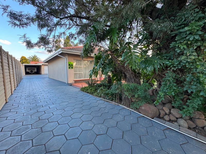 Front exterior view featuring a paved driveway, established garden, and a covered carport area.