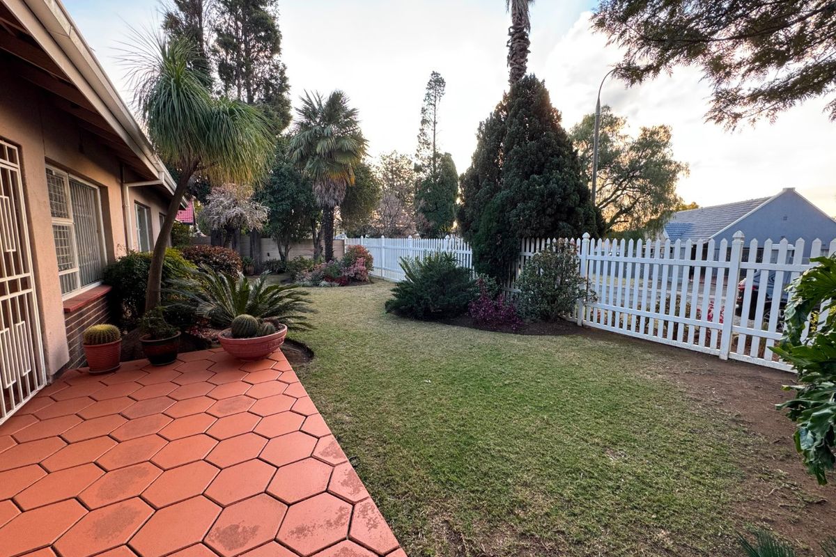 A well-maintained rear garden featuring a hexagonal paved patio, a lush lawn, and a white picket fence boundary.