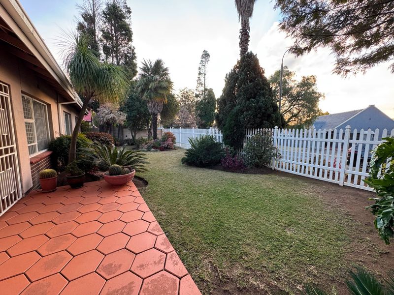 A well-maintained rear garden featuring a hexagonal paved patio, a lush lawn, and a white picket fence boundary.