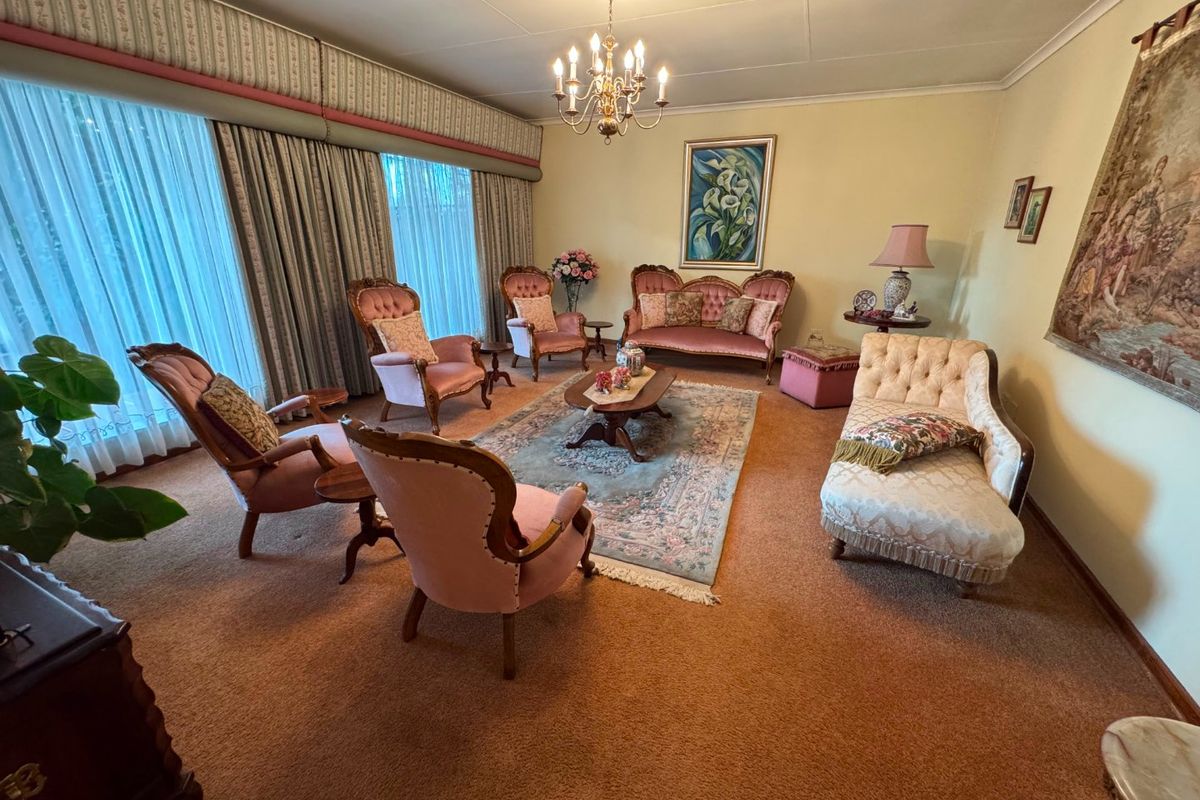 A formal living room featuring wall-to-wall carpeting, a central chandelier, and large windows with integrated curtain pelmets.