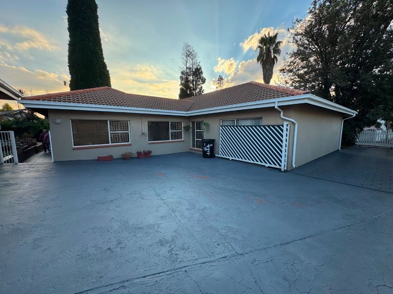 Rear exterior view of the house featuring a tiled roof, security-fitted windows, and a large paved driveway area.