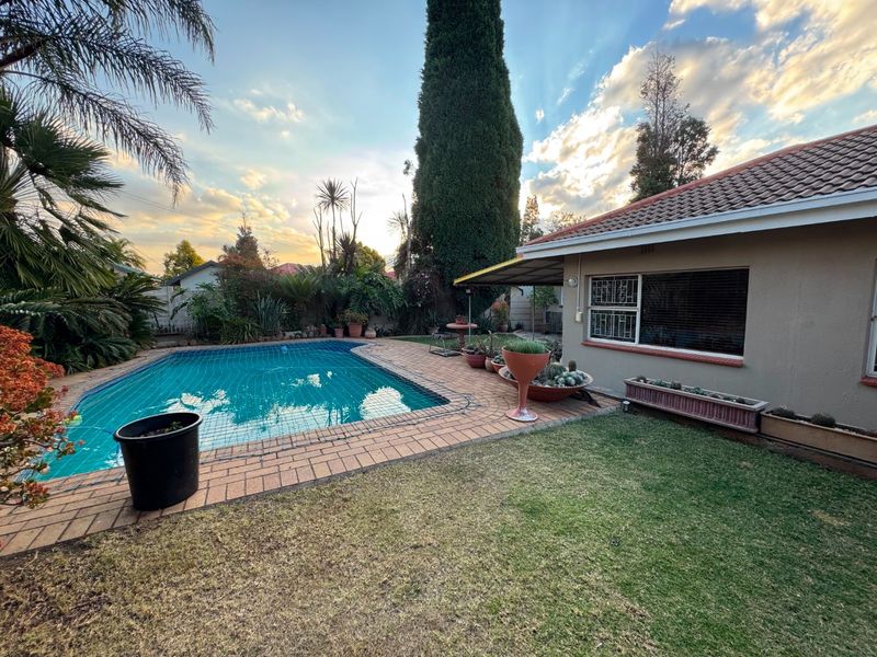 Rear garden area featuring a swimming pool with safety net, brick paved surround, and established landscaping adjacent to the main house structure.