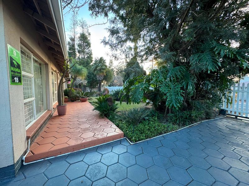 A well-maintained rear exterior featuring a tiled patio, paved area, and established garden with mature trees and shrubs.