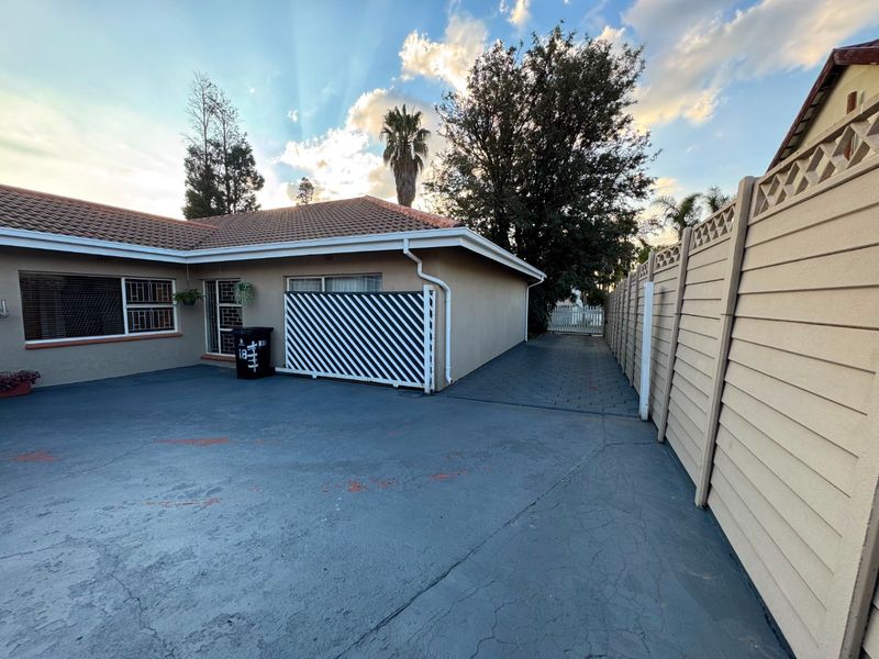Rear exterior view of the property featuring a paved driveway, boundary wall, and tiled roof structure.