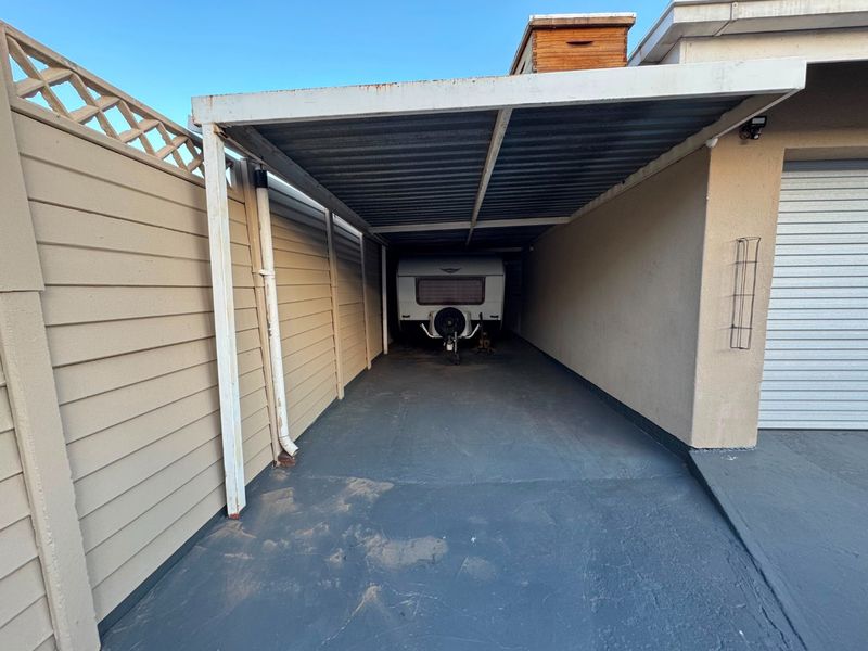 A covered carport area adjacent to the main garage, featuring a concrete floor and boundary wall enclosure.