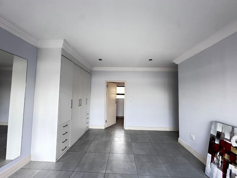 A spacious, neutral-toned bedroom featuring large-format floor tiles, extensive built-in cabinetry, crown molding, and recessed lighting.