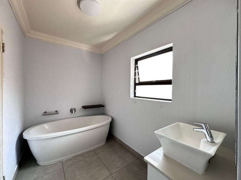 A clean, modern bathroom featuring a freestanding bathtub, a contemporary vessel sink, tiled flooring, and crown molding.