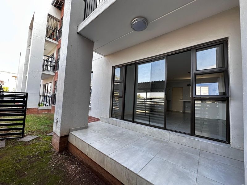 A ground-floor patio area featuring tiled flooring, a concrete support pillar, and large sliding glass doors providing access to the apartment interior.