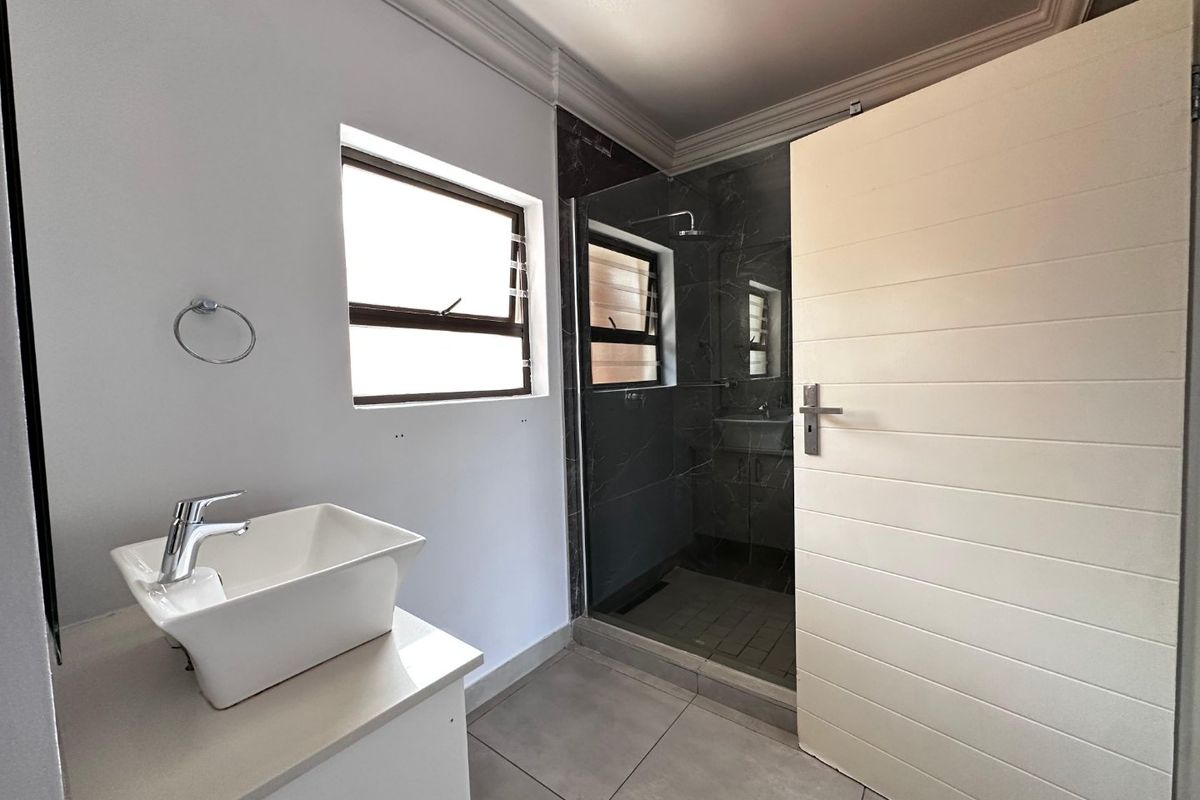 Modern bathroom featuring a vessel sink on a vanity, a glass-enclosed shower with dark tiling, and neutral floor tiles.