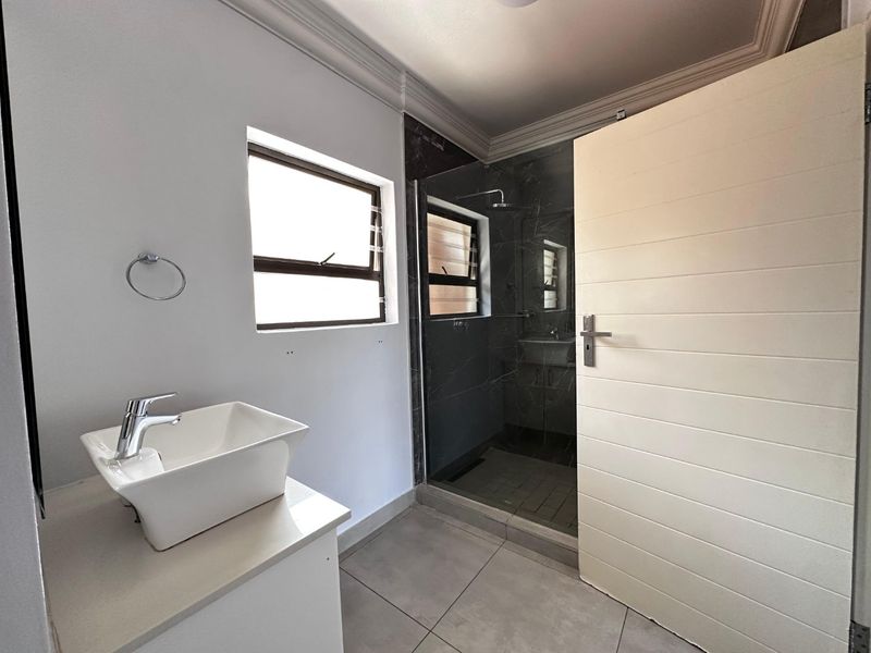 Modern bathroom featuring a vessel sink on a vanity, a glass-enclosed shower with dark tiling, and neutral floor tiles.