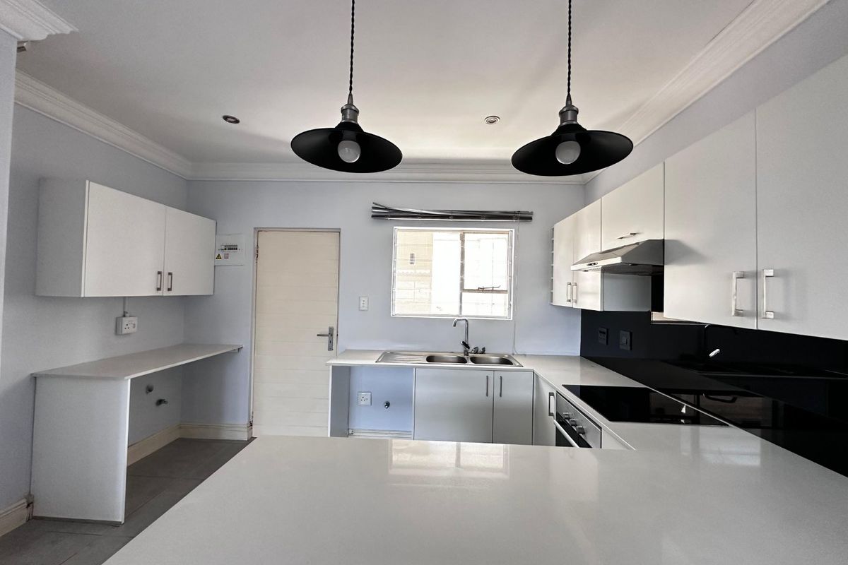 Modern kitchen featuring white cabinetry, quartz countertops, integrated appliances, and stylish pendant lighting in a clean, open layout.