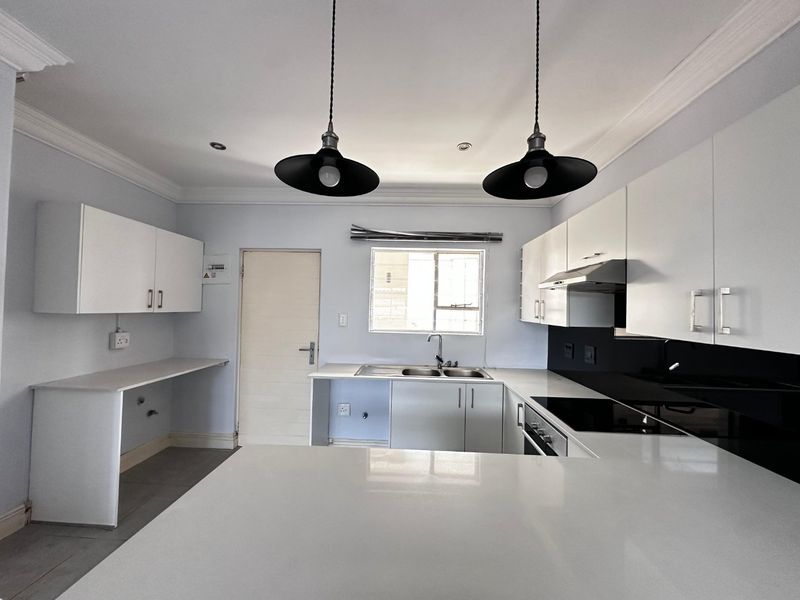 Modern kitchen featuring white cabinetry, quartz countertops, integrated appliances, and stylish pendant lighting in a clean, open layout.