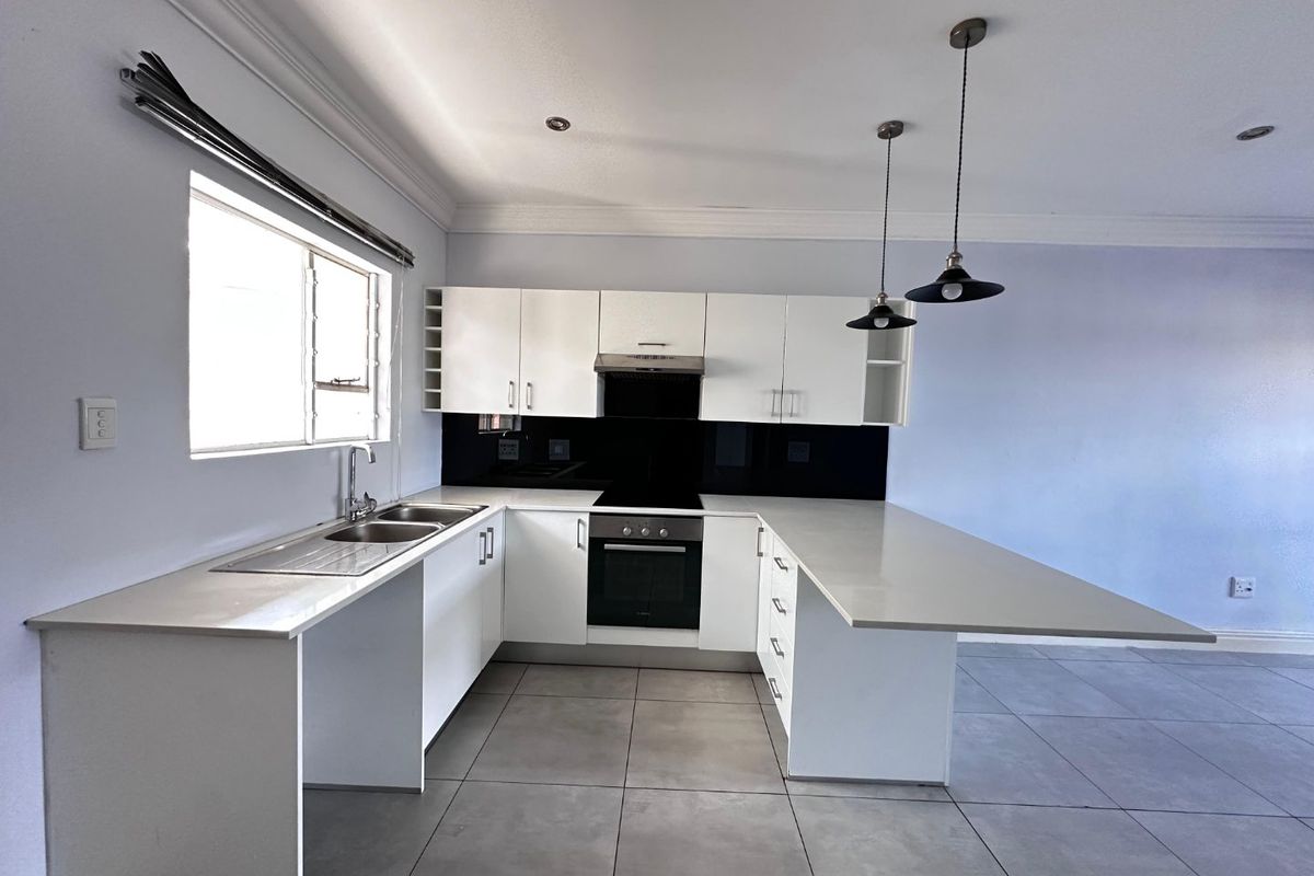 Modern kitchen featuring white cabinetry, stone countertops, integrated oven and hob, and a breakfast bar peninsula with pendant lighting.