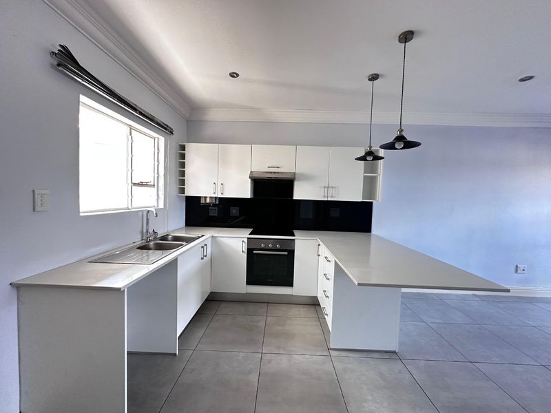 Modern kitchen featuring white cabinetry, stone countertops, integrated oven and hob, and a breakfast bar peninsula with pendant lighting.