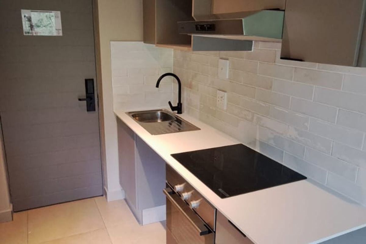 Modern compact kitchen featuring sleek cabinetry, integrated electric hob, oven, extractor fan, subway tile backsplash, and contemporary track lighting.