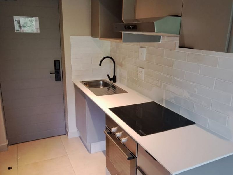 Modern compact kitchen featuring sleek cabinetry, integrated electric hob, oven, extractor fan, subway tile backsplash, and contemporary track lighting.