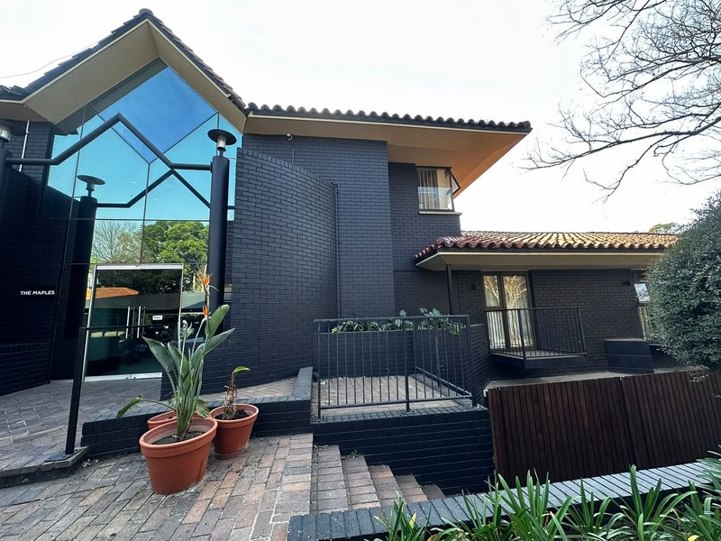 Front elevation of The Maples apartment complex featuring a modern glass facade, dark painted brickwork, and tiled roofing with external stair access.
