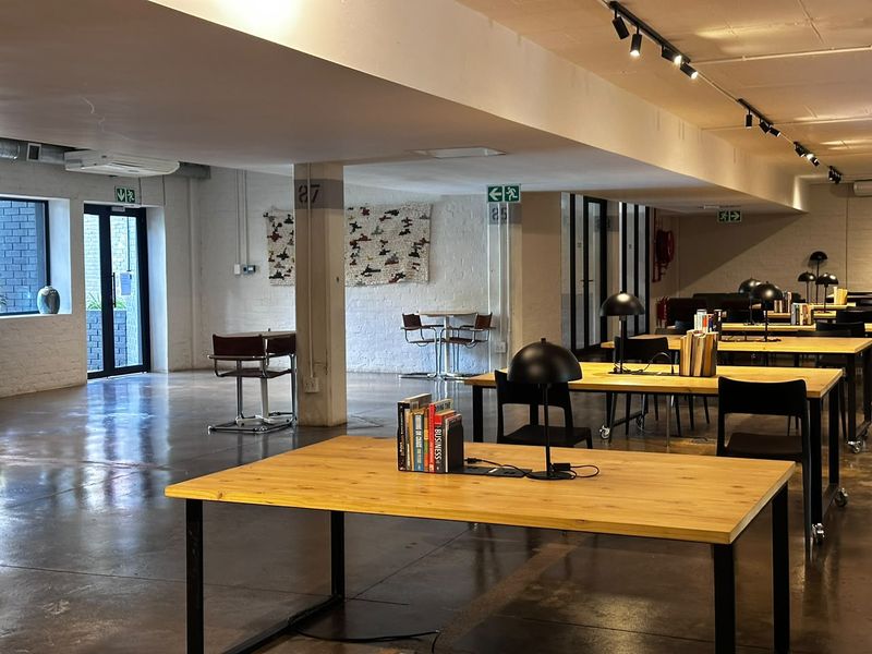 A spacious, modern open-plan office area featuring polished concrete floors, industrial-style track lighting, and large glass doors providing natural light.