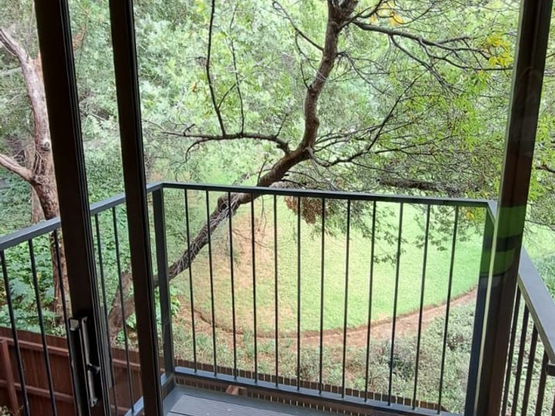 A compact balcony featuring modern composite decking and a metal safety railing, offering a peaceful view of the surrounding trees and garden area.