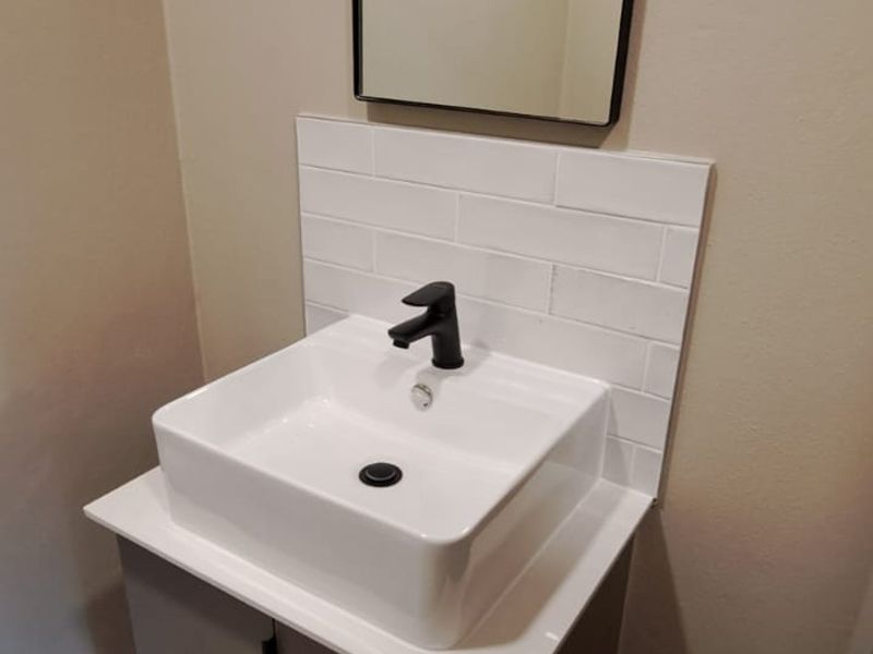 A modern bathroom vanity featuring a white vessel sink, black faucet, subway tile backsplash, and a sleek wall-mounted cabinet.