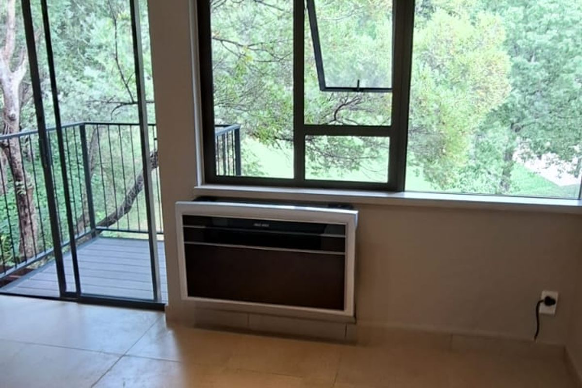 Bright and spacious living area featuring neutral tiled flooring, modern track lighting, a wall-mounted air conditioner, and direct access to a private balcony.