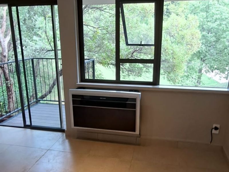 Bright and spacious living area featuring neutral tiled flooring, modern track lighting, a wall-mounted air conditioner, and direct access to a private balcony.