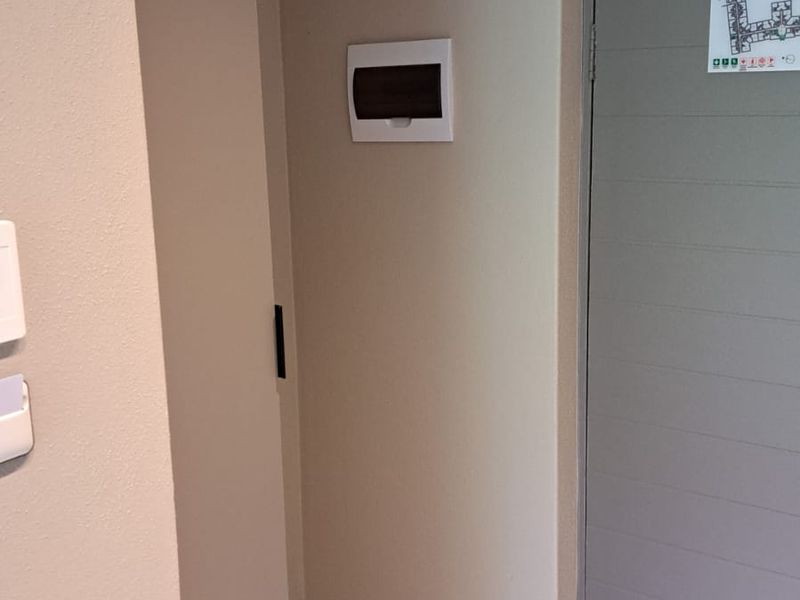 A clean, neutral-toned hallway featuring a secure fire door with a door closer and a wall-mounted electrical distribution board.