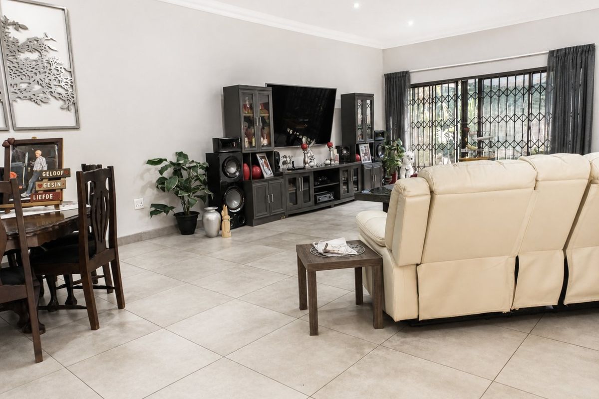 Spacious living area featuring neutral tiled flooring, recessed downlighting, and large sliding glass doors with security gates leading to the exterior.